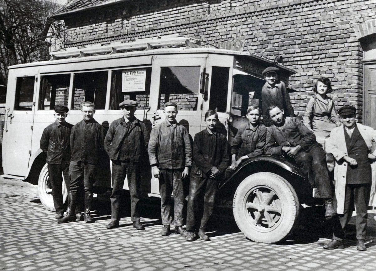 Altes Schwarzweiß-Bild von mehreren Personen vor einem Auto 1929