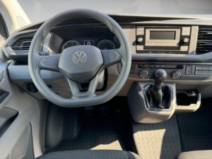 Innenansicht eines grauen Volkswagen-Armaturenbretts mit Lenkrad und Schalthebel, Sonnenlicht.