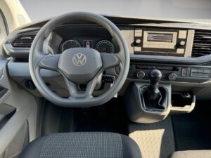 Innenraum eines VW-Fahrzeugs mit grauem Lenkrad und Cockpit, Schalthebel und Armaturenbrett.