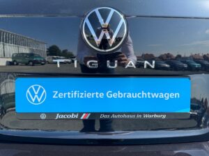 VW Tiguan-Heckklappe mit blauem Schild "Zertifizierte Gebrauchtwagen", Straße im Hintergrund.