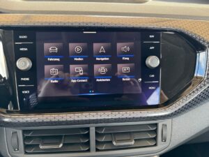 Navigationssystem in Auto mit Touchscreen, schwarz, reflektiert Licht; zeigt diverse Medien-Icons.