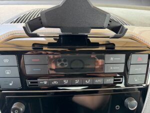 Schwarz glänzendes Bedienfeld im Auto mit Knöpfen und Reflektion eines Smartphones.