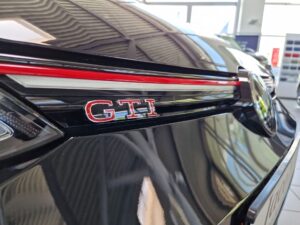 Nahaufnahme eines schwarzen GTI-Fahrzeugs mit glänzendem Lack und roten GTI-Emblem-Details.