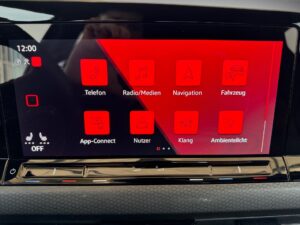 Displayscreen im Auto, zeigt rote Menüsymbole an, darunter Telefon, Navigation und Klang.