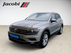 Silberner Volkswagen SUV in einem Showroom, frontale Ansicht mit Logo im Hintergrund.