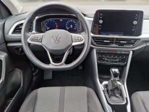 Innenraum eines VW-Autos mit grauem Lenkrad und digitalem Display, Schalthebel vorne sichtbar.