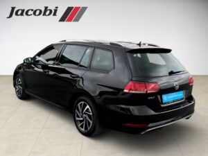 Schwarzer VW Golf Kombi seitlich, stilvoll präsentiert im Showroom mit Jacobi-Logo oben links.