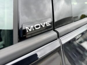 Außenansicht eines schwarzen Autos mit "MOVE"-Schriftzug und leicht bewölktem Himmel im Hintergrund.