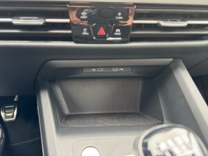 Mittelkonsole eines Autos mit schwarzen Knöpfen, USB-Anschlüssen und einer leeren Ablagefläche.