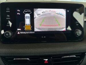 Rückfahrkamera-Display im Auto zeigt Parkplatzansicht mit Leitlinien. Bildschirm in Schwarz.