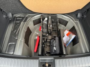 Der Kofferraum eines Autos mit Ersatzreifen-Fach, Batterie und roten Werkzeugen, geöffnet.