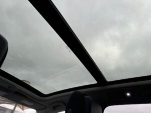 Panoramadach eines Autos unter bewölktem Himmel, dunkle Innenfarbe, moderne Ausstattung.