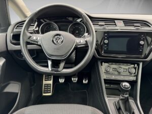 Lenkrad eines Autos mit Volkswagen-Logo, schwarzes Interieur, moderne Armaturen und Schalthebel.