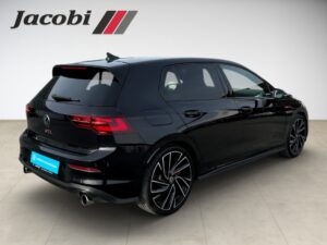 Ein schwarzer VW Golf GTI steht in einem Showroom, Seitenansicht, mit roten Rücklichtern.