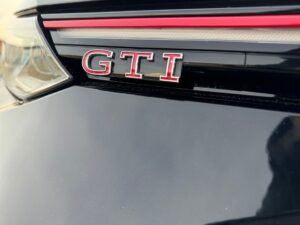 Nahaufnahme eines schwarzen Autos mit rotem "GTI"-Emblem und sportlichem Dekor.