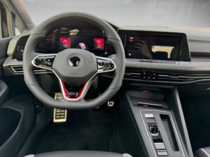 Lenkrad und Armaturenbrett eines modernen Autos mit digitalem Display, schwarz und rot gestaltet.