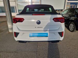 Rückansicht eines weißen VW T-Roc mit offenem Dach in einem Parkplatz.