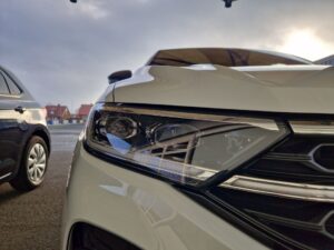 Weiße Motorhaube und Scheinwerfer eines Autos bei bewölktem Himmel.