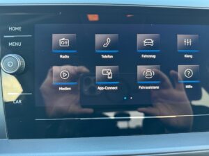 Touchscreen im Auto mit App-Symbolen, schwarz-graues Interface, leicht spiegelnde Oberfläche.