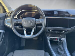 Innenraum eines Audi mit schwarzem Lenkrad, modernem Armaturenbrett und großem Touchscreen.