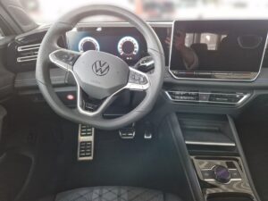 Lenkrad eines modernen VW-Autos, mit digitalem Display und schwarzem Interieur.