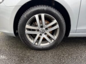 Silberne Autofelge mit Continental-Reifen auf grauem Straßenbelag.