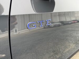 Nahaufnahme eines grauen Fahrzeugs mit blauer "GTE"-Plakette, reflektierende Oberfläche.