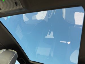 Autodach mit Panoramaglas, blauer Himmel, Reflexionen auf Sitzen, moderne Innenansicht.