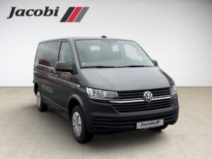 Ein grauer Volkswagen-Transporter, Frontalansicht, im Hintergrund das Logo "Jacobi".