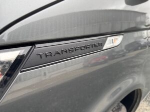 Graues Fahrzeug mit "Transporter"-Logo, kantiger Scheinwerfer, glänzende Lackfarbe.