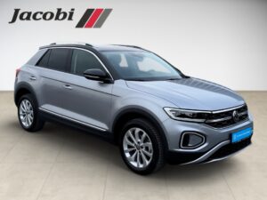 Silberner VW T-Roc in Seitenansicht, grauer Boden, Logo oben links.