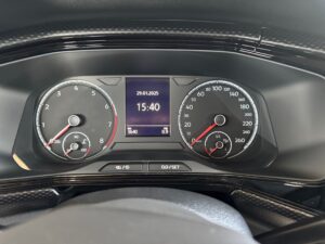 Tacho-Display eines Autos mit Uhrzeit und Datum, schwarze Anzeige mit weißen und roten Details.