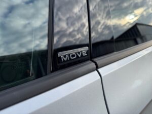 Nahaufnahme eines silbernen Autos mit „MOVE“-Emblem, Spiegelung des Himmels auf der Scheibe.