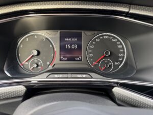 Nahaufnahme eines Fahrzeugtacho-Displays mit analogen Anzeigen und digitaler Uhrzeit in der Mitte.