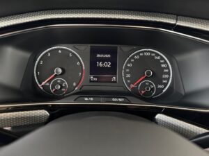 Nahaufnahme eines Autotachometers mit digitalen Anzeigen, schwarzes Armaturenbrett, rote Nadeln.