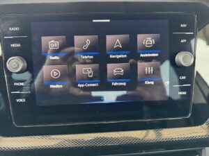 Touchscreen-Autoradio mit Reflektion von Händen, zeigt Menüs für Radio, Telefon, Navigation.