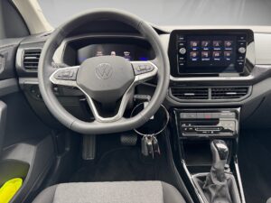 Innenraum eines Autos mit VW-Lenkrad und Infotainment-Bildschirm, neutrale Farben, modernes Design.