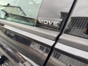 Schwarzes Auto mit dem Emblem "MOVE" an der Tür, reflektiert Gebäude.