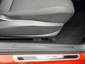 Grauer Autositz, Türschwelle mit "UNITED"-Schriftzug, rote Fahrzeugkarosserie.