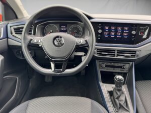 Innenansicht eines modernen Autos mit VW-Logo, graues Armaturenbrett, Infotainment-Bildschirm.