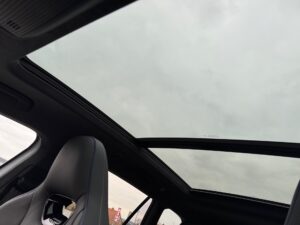 Panoramadach eines Autos mit wolkigem Himmel darüber, Fenster geöffnet, graue Innenverkleidung.