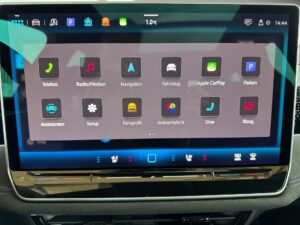 Ein Auto-Infotainment-Bildschirm mit verschiedenen Apps auf einem grauen Hintergrund.