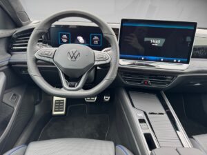 Lenkrad und Bildschirme eines modernen VW-Fahrzeugs, schwarzes Interieur mit blauen Akzenten.