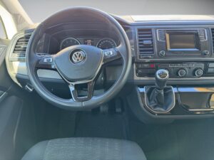 Innenraum eines VW mit Lenkrad, Armaturenbrett und Schalthebel; modernes Design in Schwarz.