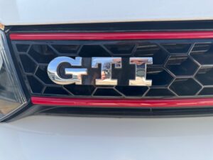 Nahaufnahme eines GTI-Emblems auf einem weißen Auto mit rotem Akzent.