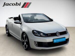 Weißer VW Golf Cabrio mit geöffnetem Verdeck, GTI-Emblem und markanten Felgen.