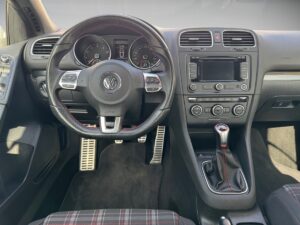 Armaturenbrett eines Volkswagen-Autos, schwarzes Interieur, rotes Lenkrad-Detail, Schaltknüppel.