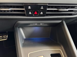 Auto-Mittelkonsole mit Warnblinkschalter, Klimaanlage und USB-Anschlüssen, schwarze Farbgebung.