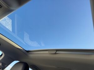 Autoschiebedach im offenen Zustand, blauer Himmel sichtbar, Innenraum des Autos in neutralen Farben.