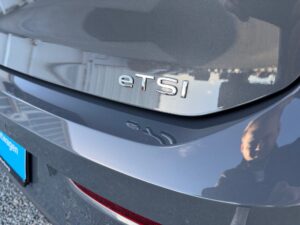 Rückseite eines grauen Autos, eTSI-Logo, Spiegelung einer Person im Lack.